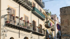 Une rue étroite bordée d’immeubles dotés de balcons ornés de plantes et d’espaces aménagés pour s’asseoir à l’extérieur.