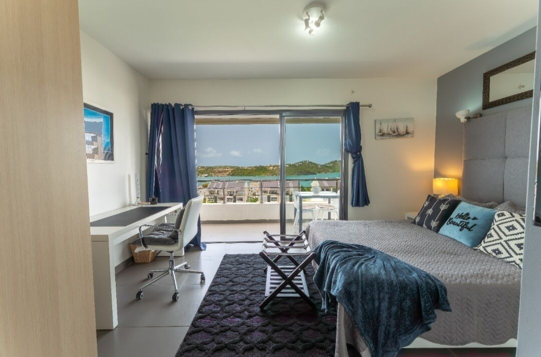 Een hotelkamer met een bed, een bureau, een stoel, een bijzettafeltje en uitzicht op zee.