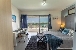 Quarto de hotel com cama, escrivaninha, cadeira, mesinha e vista para o mar.