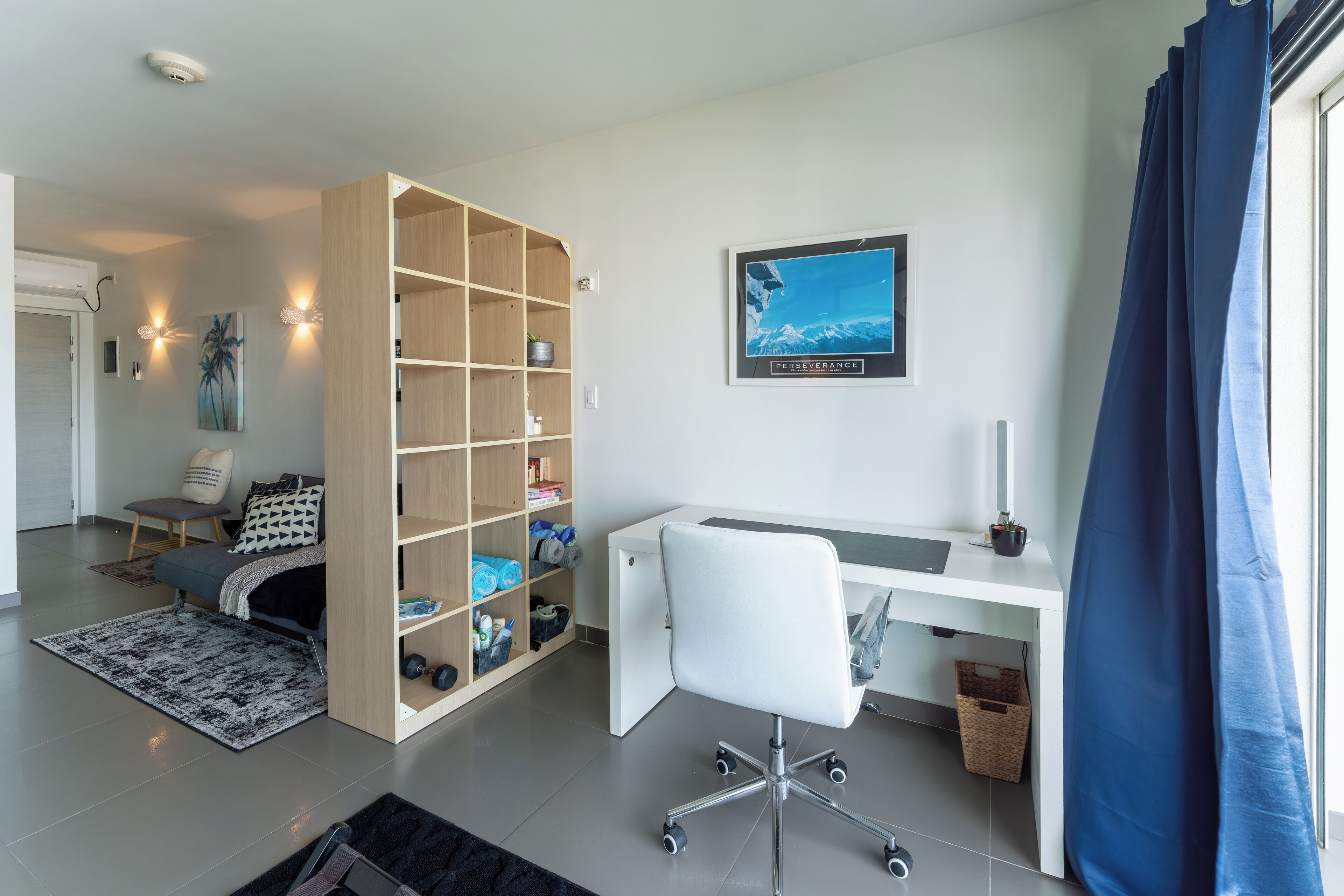 Ett modernt rum med ett skrivbord, en stol, en bokhylla och ett stort fönster med gardiner.