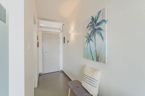 A hallway with a door, a bench, and a wall-mounted light fixture. - Lowlands Condo-NearPrincessJulianaAirport-Beaches (Sint Maarten)