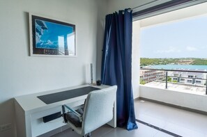 Una habitación moderna con escritorio, silla y un amplio ventanal con vistas al agua y edificios.