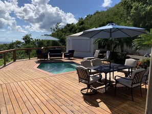A wooden deck with a pool, outdoor furniture, and a view of the ocean.