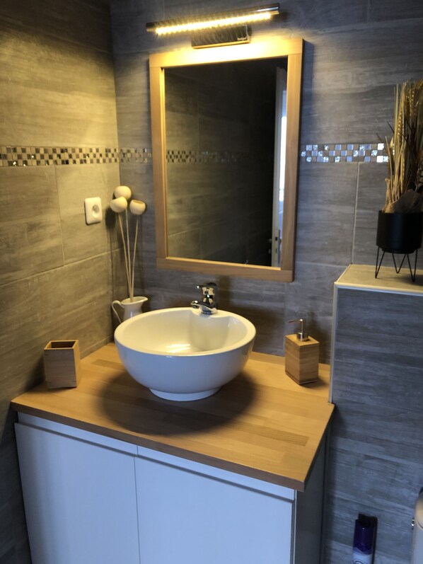 Un baño moderno con un lavamanos grande de color blanco, un espejo y una encimera de madera.
