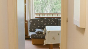 A hallway leading to a room with a sofa and a table, a window with curtains, and a view of trees.