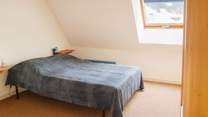 A small, single-bed room with a sloped ceiling and a window overlooking a snowy landscape.