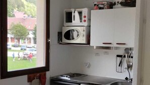 Una cocina compacta con armarios blancos, microondas integrado, estufa y ventana con vistas a un barrio residencial.