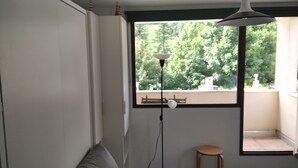 Una habitación con un ventanal grande, una lámpara de pie, un taburete pequeño y un banco en el exterior.