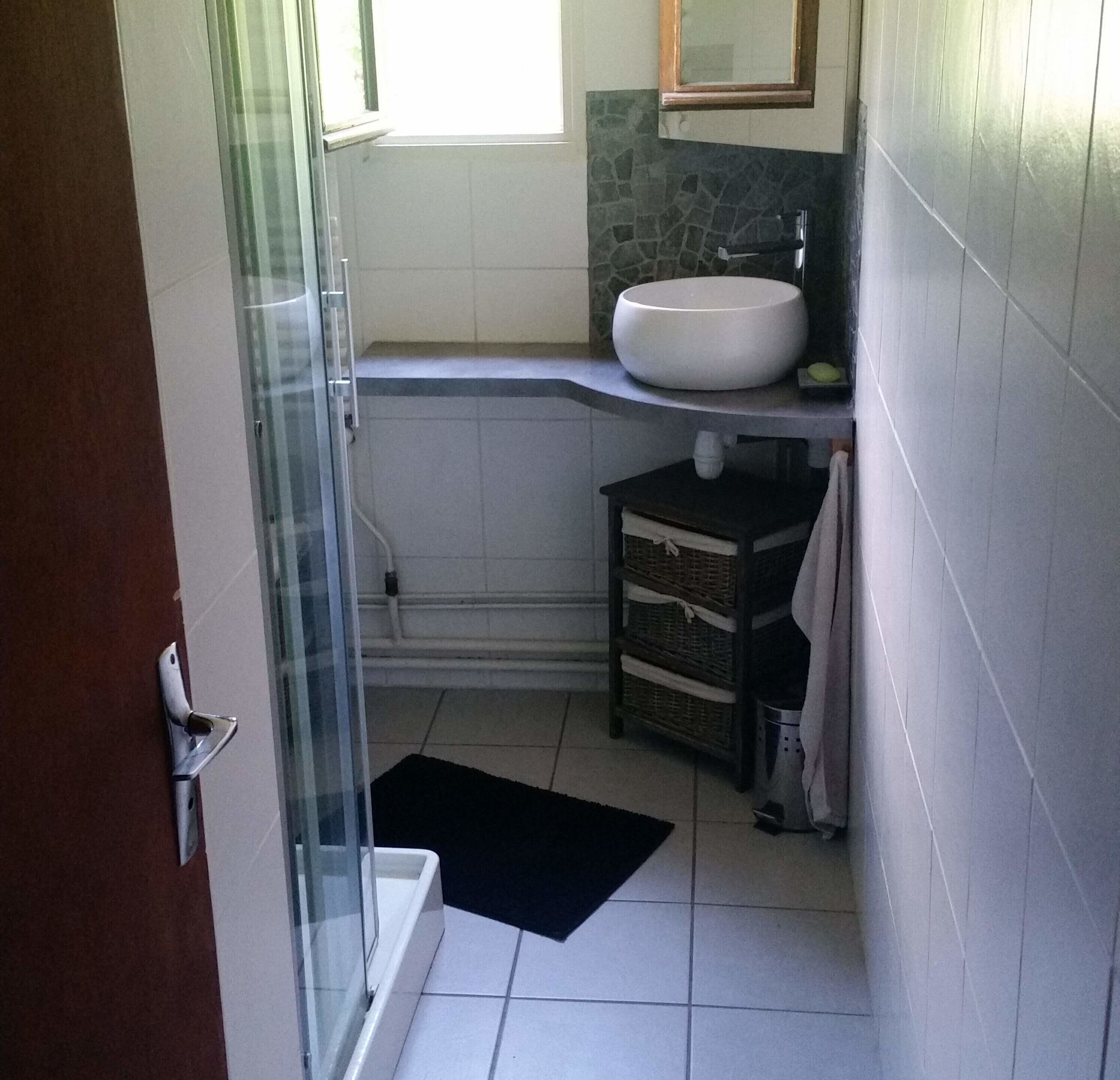 A bathroom with a glass shower enclosure, a white sink, a tiled floor, and a small wicker basket.