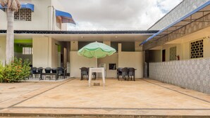 A covered outdoor patio with a table and chairs, a green umbrella, and a palm tree. - Pousada Vilas Costeira (São Luís)
