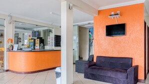 A reception area with a counter, a sofa, and a TV mounted on the wall. - Pousada Vilas Costeira (São Luís)