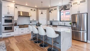 Una cocina moderna con armarios blancos, electrodomésticos de acero inoxidable, una isla central con taburetes de bar e iluminación colgante.