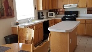 A kitchen with wooden cabinets, a microwave, a stove, and a dining area with a table and chairs. - Great for ATV's and TOY'S!  Rent 6 nights and 7th is free! (Buena Vista)
