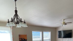 A dining area with a wooden table, chairs, and a chandelier. There is a sofa and a television in the background. - Great for ATV's and TOY'S!  Rent 6 nights and 7th is free! (Buena Vista)
