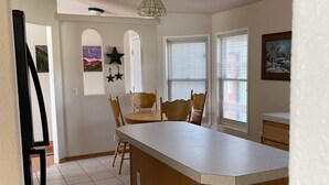 A kitchen with a central island, wooden chairs, a dining table, and a window with blinds. - Great for ATV's and TOY'S!  Rent 6 nights and 7th is free! (Buena Vista)