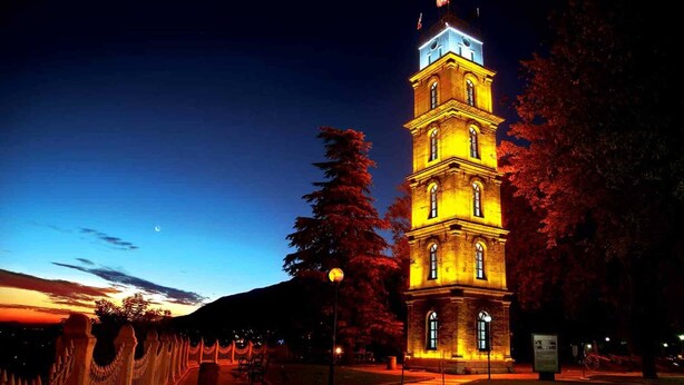 Un edificio histórico con una torre y un reloj en la parte superior, rodeado de árboles y una cerca.