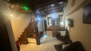 Zona de recepción de un hotel con mostrador, escalera y área de estar.