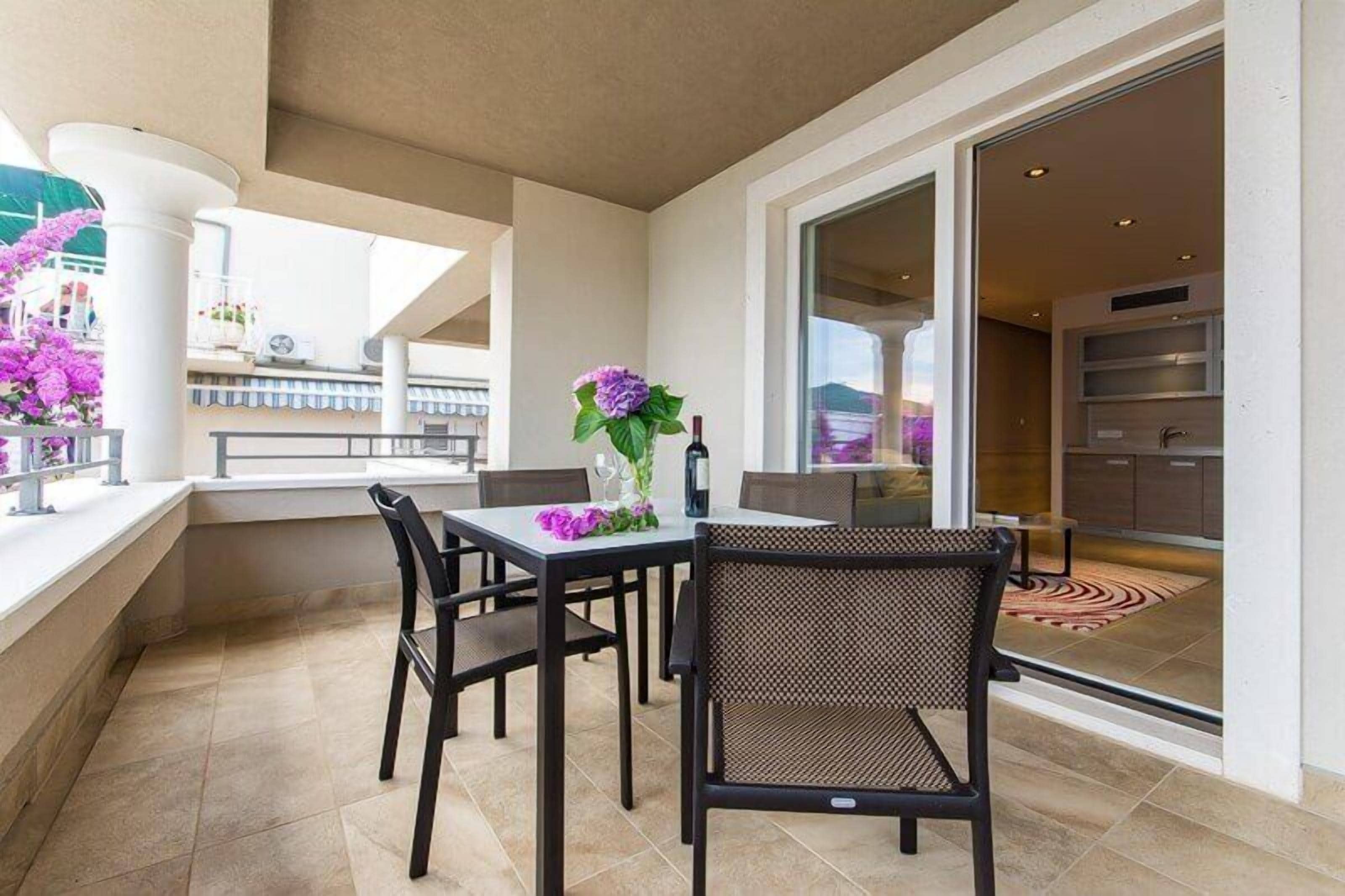 A balcony with a table and chairs, a vase with flowers, and a view of the interior.