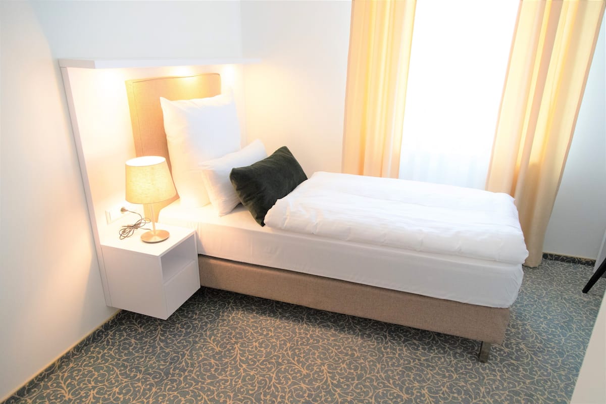 A neatly made bed with white linens, a bedside lamp, and a patterned carpet.