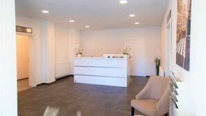 A reception area with a white reception desk, a beige armchair, and a large poster on the wall. - Amplidi Hotel Hannover (Hannover)