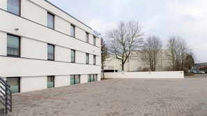 A modern building with a flat facade, multiple windows, and a paved courtyard. - Amplidi Hotel Hannover (Hannover)