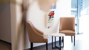 A modern interior with two brown chairs and a small table, a wall-mounted magazine rack, and a large window providing natural light. - Amplidi Hotel Hannover (Hannover)