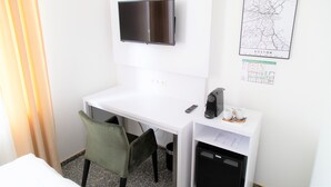 A hotel room with a white desk, a television mounted above it, a map of Boston on the wall, and a trash can under the desk. - Amplidi Hotel Hannover (Hannover)