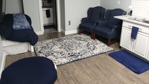 Un dormitorio con cama, sofá azul, alfombra estampada y una kitchenette con un armario blanco y una toalla azul.