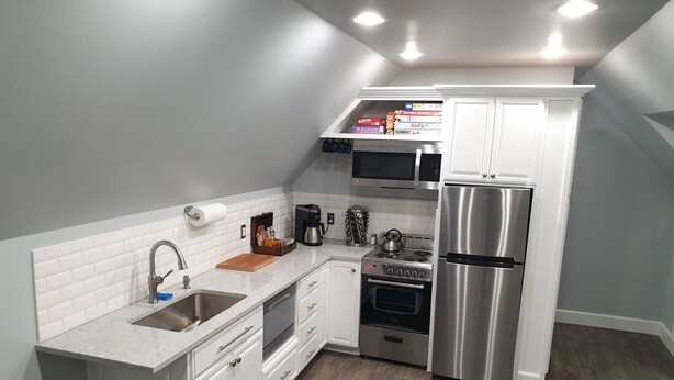 Una cocina compacta con gabinetes blancos, un refrigerador de acero inoxidable, un microondas y una estufa.