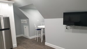 Una cocina moderna con un refrigerador de acero inoxidable integrado, un comedor con una mesa blanca y dos sillas, y un televisor de pantalla plana montado en la pared.
