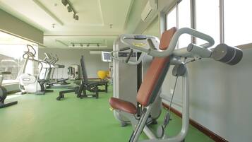 Een sportschool met trainingsapparatuur, een groene vloer en grote ramen.