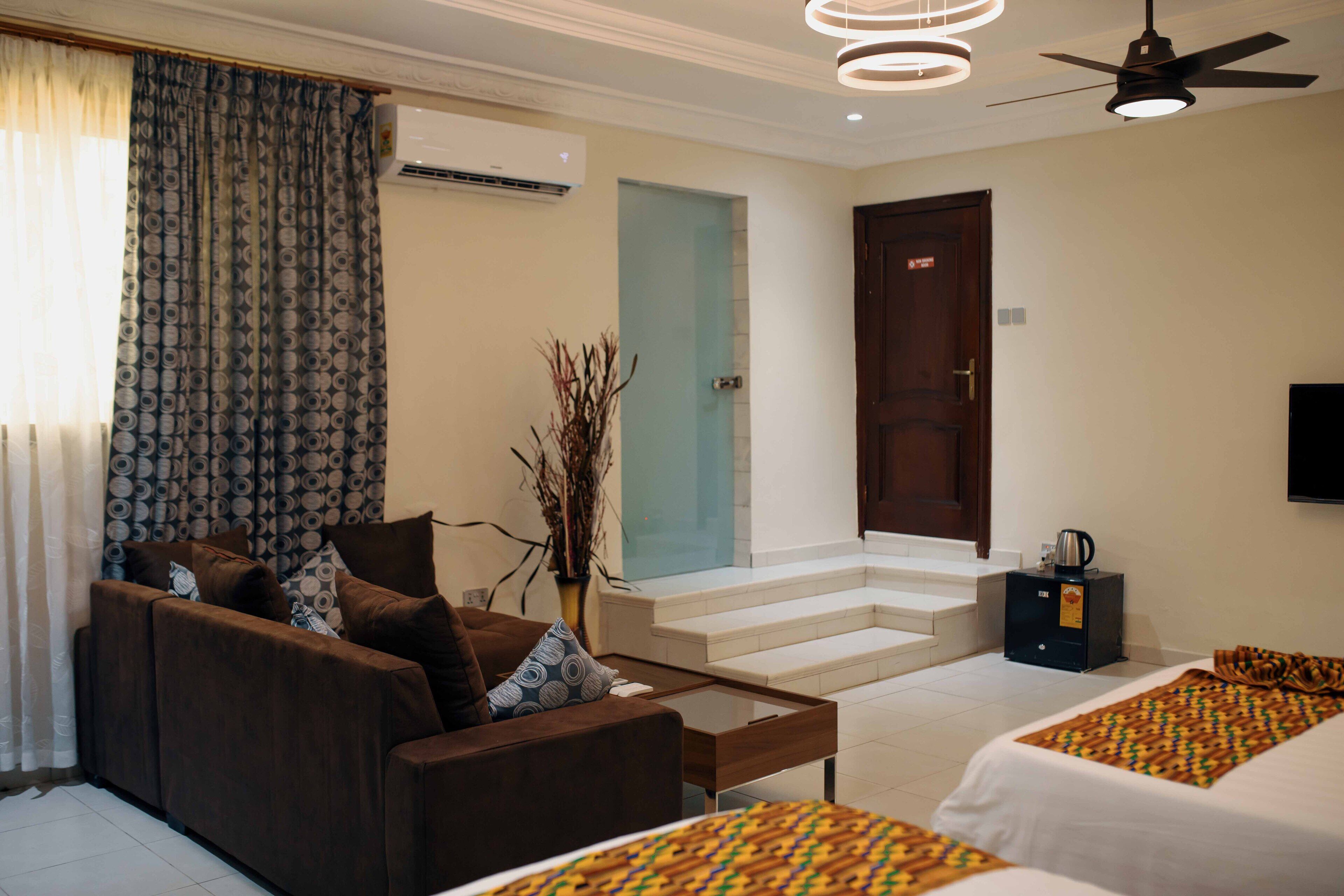 A hotel room with a sofa, two beds, a coffee table, a TV, and a staircase leading to an upper floor.