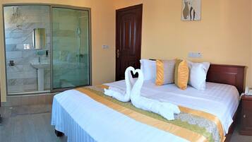 A hotel room with a bed, a wooden door, a glass shower enclosure, and a wall-mounted artwork.