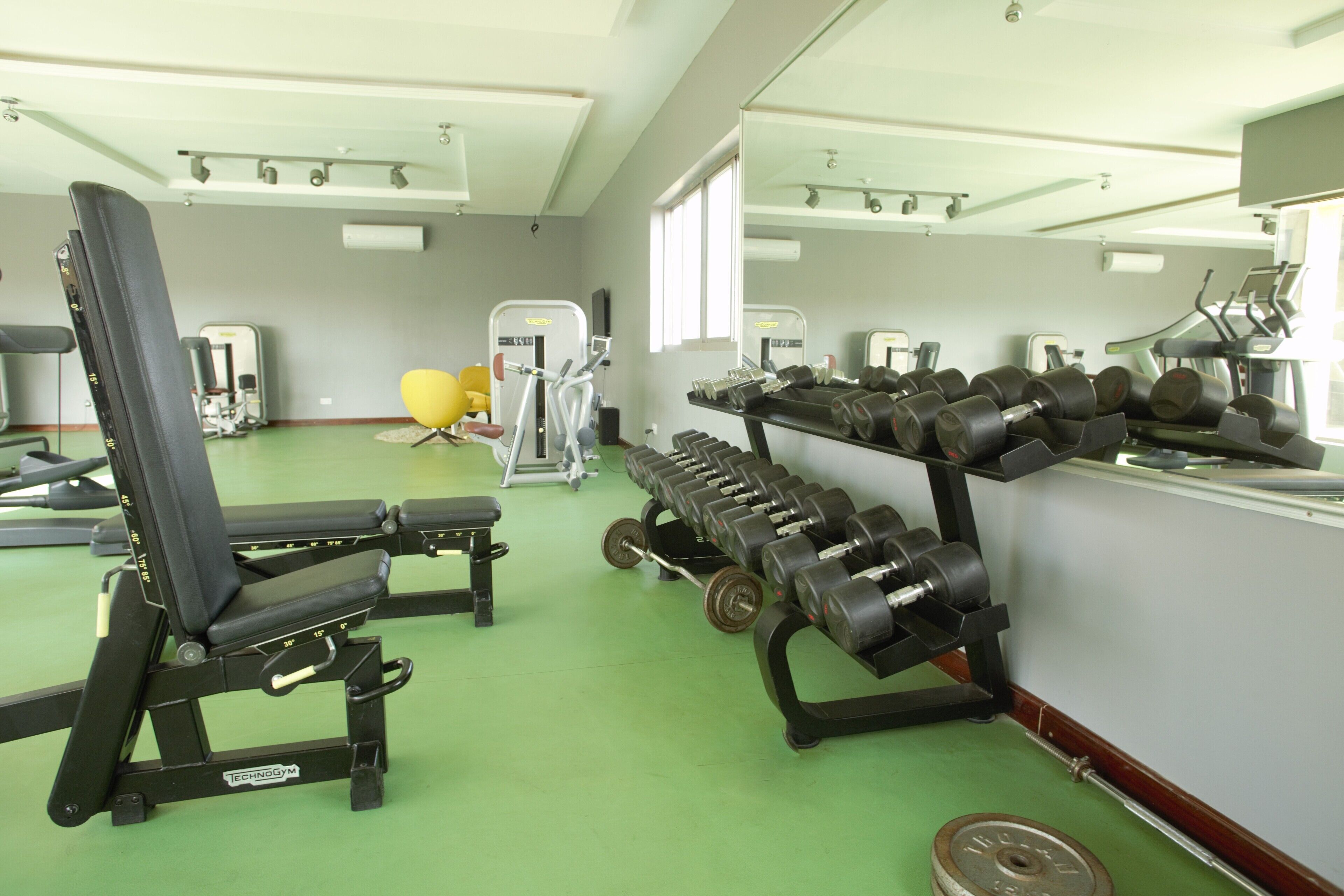 Ein Fitnessstudio mit Trainingsgeräten, Spiegeln und einem grünen Boden.