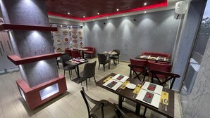 En restaurantindretning med røde og grå farver, flere spiseborde og stole.