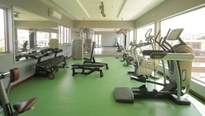 Et fitnesscenter med forskellig træningsudstyr, store vinduer og et grønt gulv.
