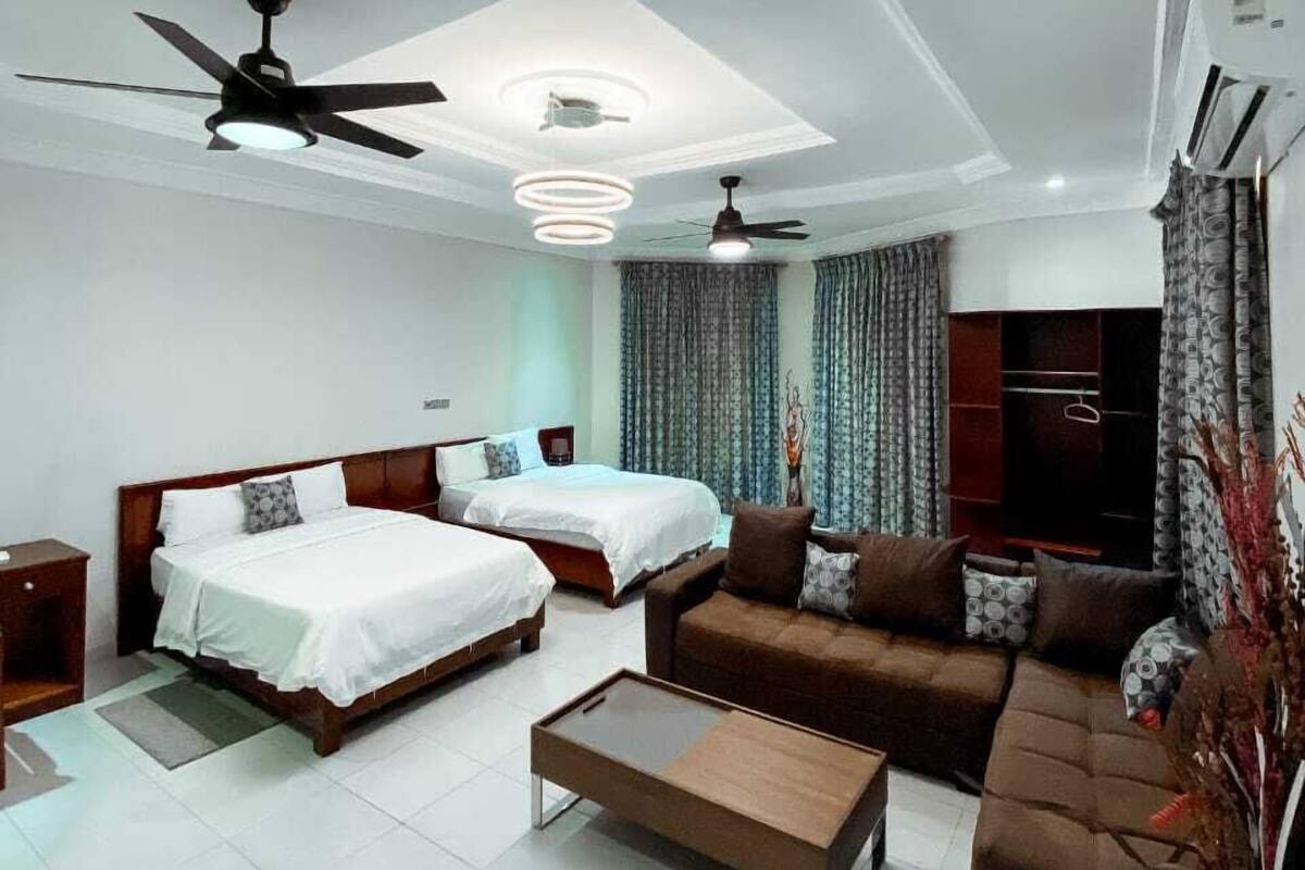 Quarto de hotel moderno com duas camas, um sofá, uma mesa de centro, ventoinha no teto e ar condicionado.