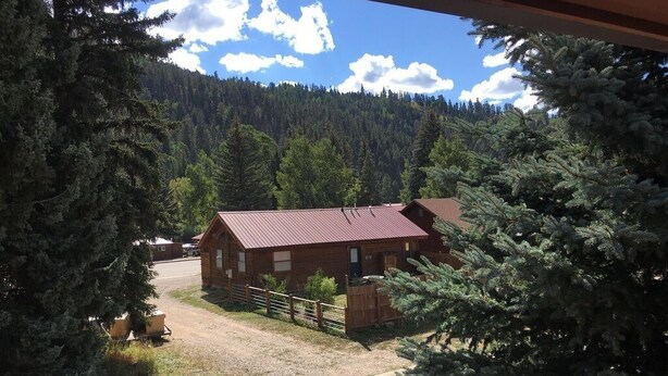 A rustic cabin with a red roof, surrounded by dense forest.