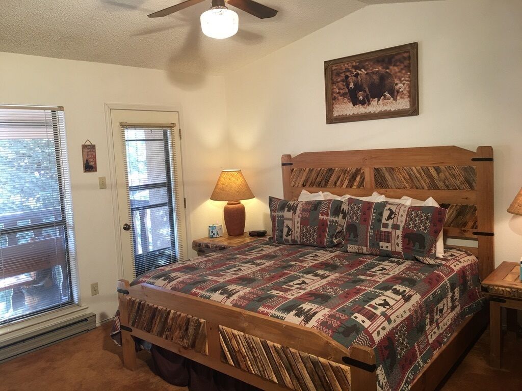 A bedroom with a wooden bed, patterned bedding, a wall-mounted lamp, and a bear-themed picture.