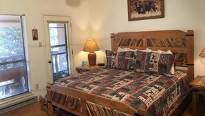 A bedroom with a wooden bed, patterned bedding, a wall-mounted lamp, and a bear-themed picture.