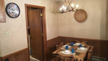 A dining area with a wooden table set for four, a clock on the wall, and a chandelier.