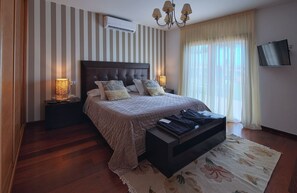 A modern bedroom with a large bed, a flat-screen TV, and a chandelier. - VILLA WITH POOL AND VIEWS (Antigua)