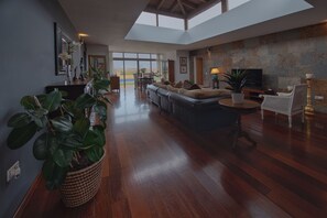 A spacious living area with a large sofa, a coffee table, and a television. There are potted plants and a view of the outdoors through large windows. - VILLA WITH POOL AND VIEWS (Antigua)
