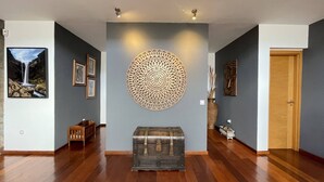 A hallway with wooden flooring, a large decorative wall piece, a framed picture, and a wooden door.