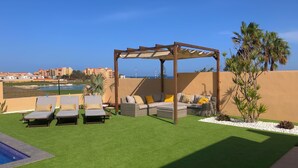 A rooftop terrace with artificial grass, lounge chairs, a wooden pergola, and a view of the city skyline.