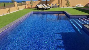 A rectangular swimming pool with clear blue water, surrounded by a well-maintained lawn and a pergola with lounge chairs.