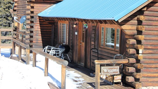 A wooden cabin with a covered porch, a grill outside, and a sign that reads "Wiggins".