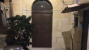A stone-paved courtyard with a double wooden door, a potted plant, and a barrel labeled "A Cantuccio." - Casa Adelina in the Center of the Sassi (Matera)