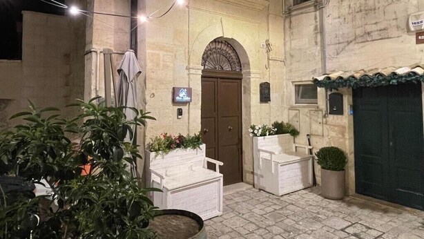 An outdoor courtyard with a stone building, a wooden door, and potted plants. - Casa Adelina in the Center of the Sassi (Matera)