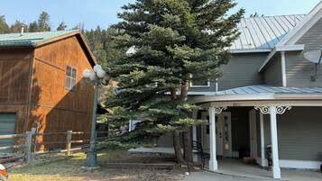 A residential property with a wooden barn, a large evergreen tree, and a covered porch.
